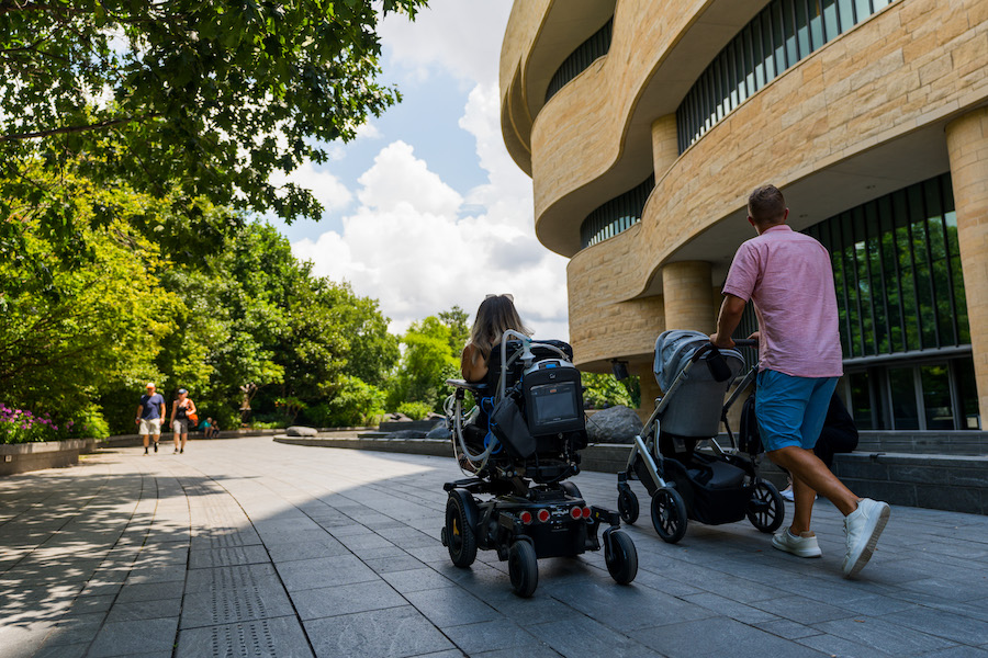 A family outside a museum, one pushing a stroller and another in a wheelchair