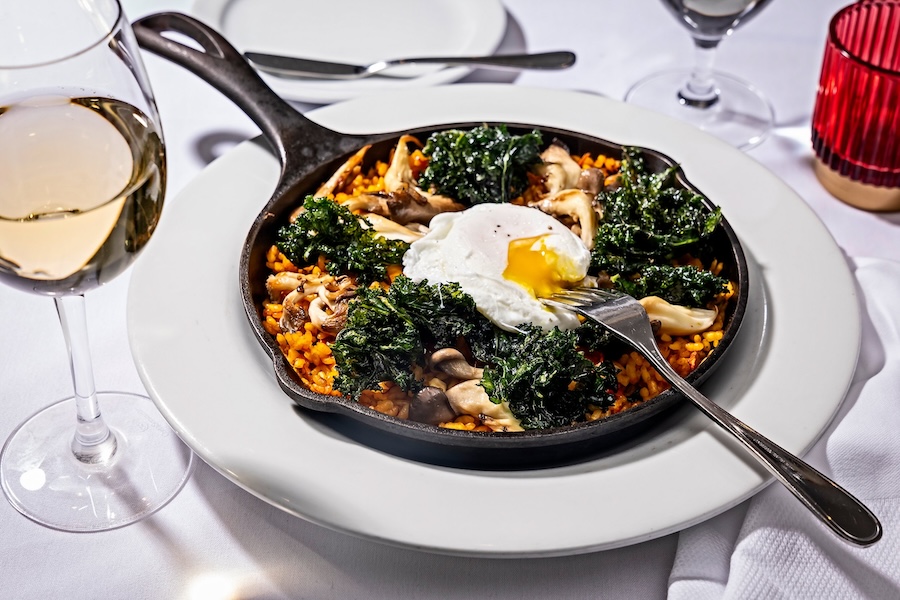 skillet with paella, kale and fresh egg on a white table spread