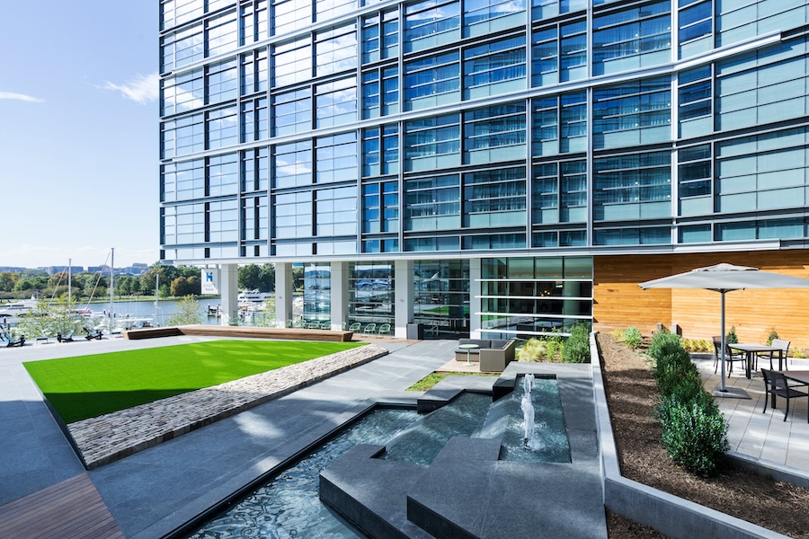 exterior courtyard with plants green space and terraced concrete seating, with a modern hotel facade in the background