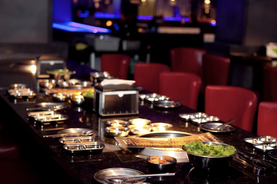 A dimly lit dining table set with metal trays and dishes, surrounded by red chairs in a cozy, intimate setting.