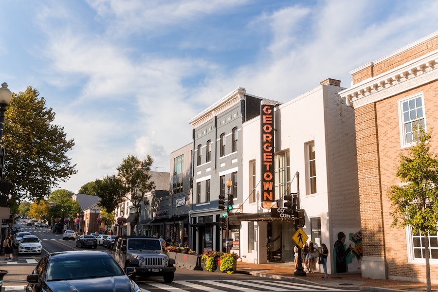 A street view of Georgetown with a mix of historical and modern buildings, including a theater with a prominent "GEORGETOWN" sign. Cars and pedestrians are visible on the street.