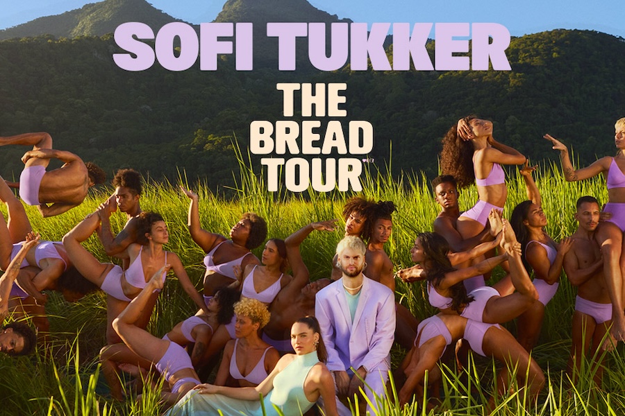 A poster for Sofi Tukker's 'The Bread Tour' featuring the duo surrounded by dancers in pink outfits, posing in a lush green field with mountains in the background.