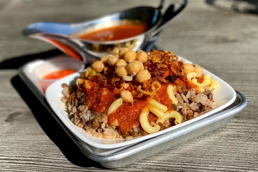 This image features koshary, an Egyptian dish made of rice, lentils, pasta, and chickpeas, topped with tomato sauce and crispy onions.