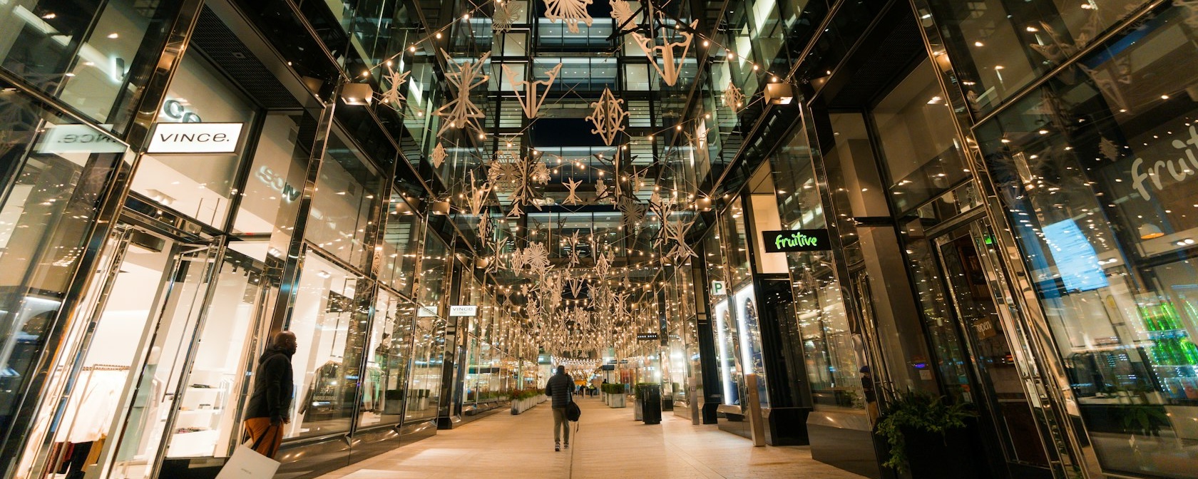 Holiday lights and star decorations adorn the high-end shopping corridor at CityCenterDC, reflecting off the glass storefronts of luxury retailers, including Vince and Fruitive.