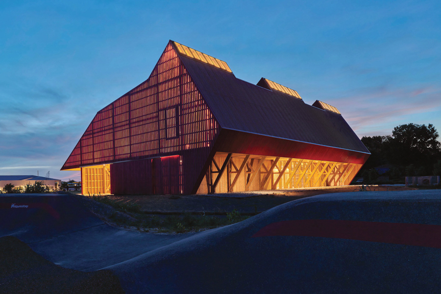 Modern barn-like building illuminated from within against a twilight sky.