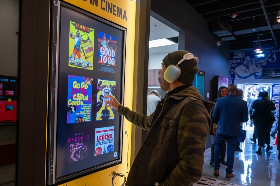 A visitor wearing headphones browses a digital display featuring classic go-go album covers in the museum.