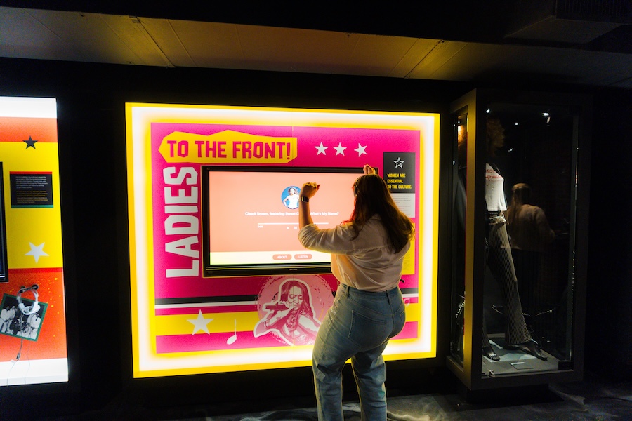 A woman interacts with a bright, immersive exhibit celebrating women in go-go music at the Go-Go Museum.