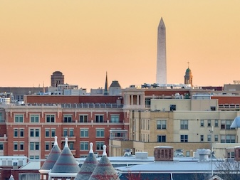 A photo of the DC skyline at sunset with the Washington Monument just beyond the historic buildings below. 
