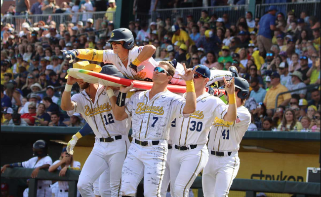 A victorious baseball team lifts a man on their shoulders in celebration, showcasing their team spirit.