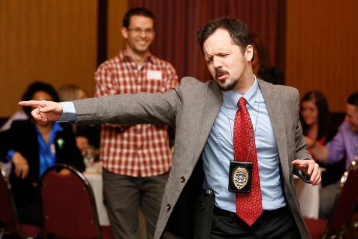 A person dressed as a detective points accusingly in a murder mystery setting.