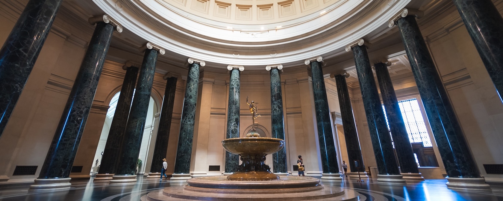 Grand rotunda of the National Gallery of Art featuring a circular fountain and towering marble columns.