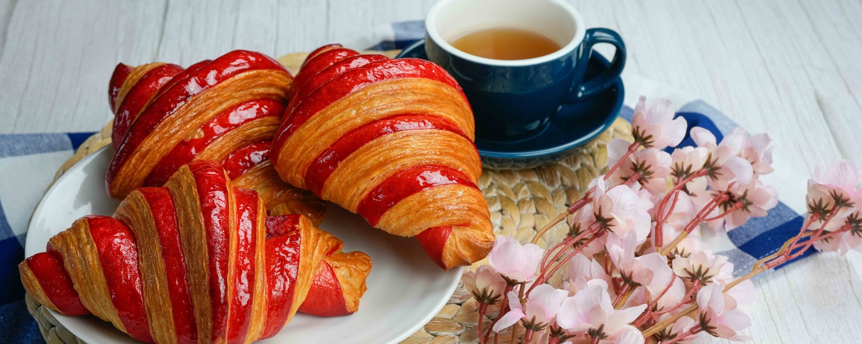 A table with quiche, sandwich, raspberry croissant, dessert, cherries and coffee.