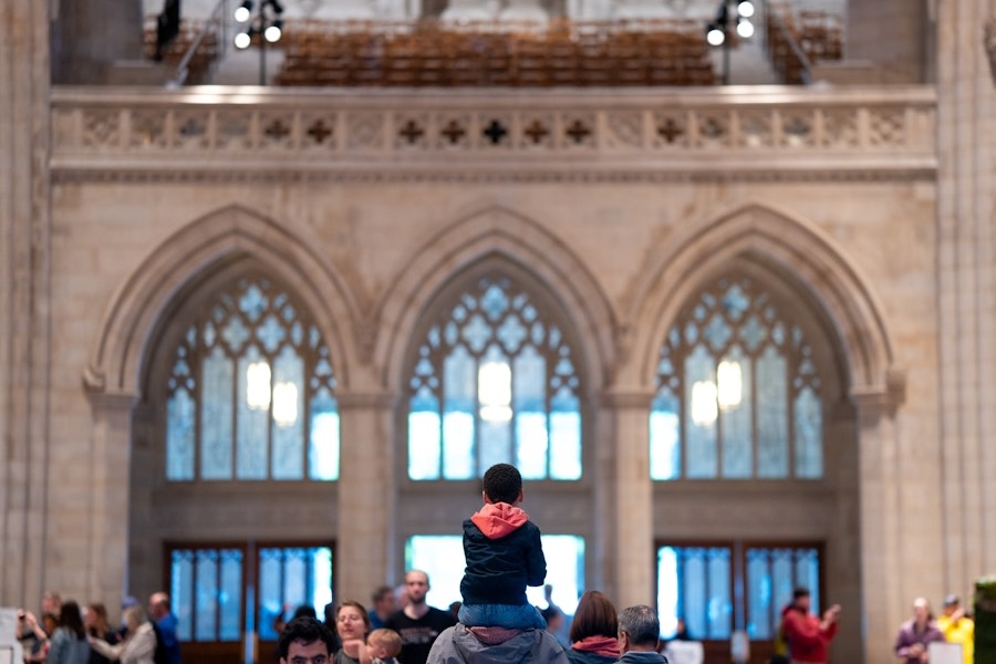 A child sits on an adult’s shoulders inside Washington National Cathedral, surrounded by visitors admiring the grand Gothic architecture.