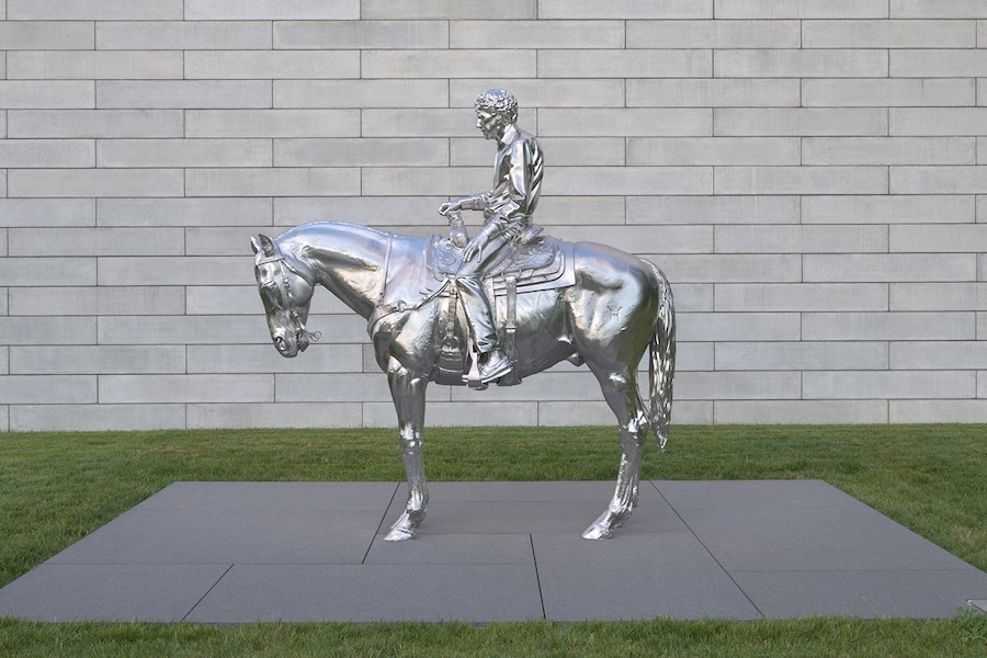 Charles Ray’s stainless steel sculpture “Horse and Rider” depicts a man on horseback outside a stone wall.