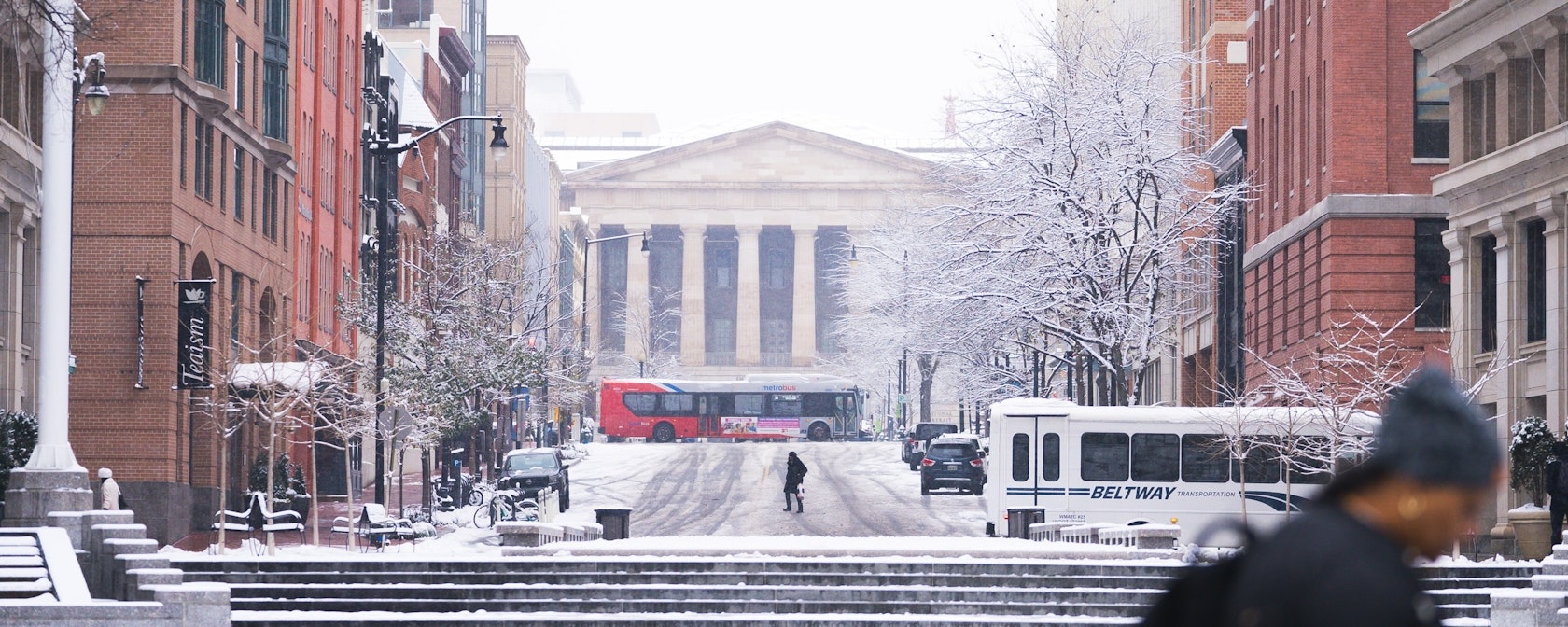 A snowy scene of a downtown street leading up to the National Archives in Washington, DC. 