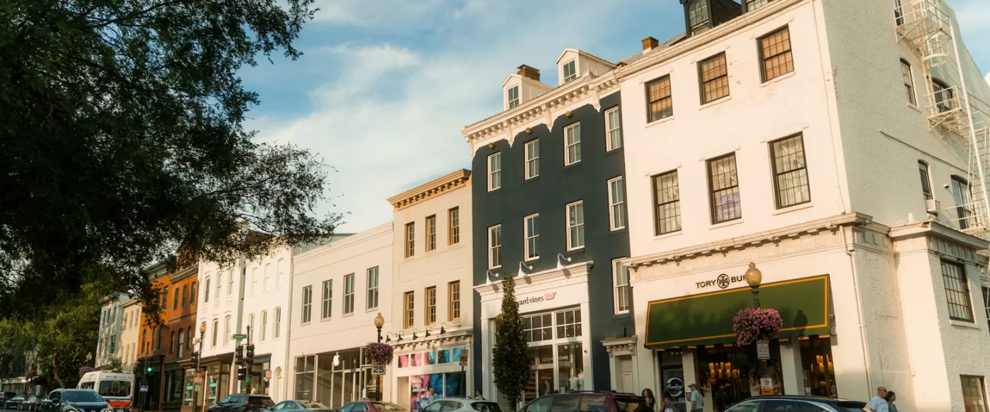 A picturesque Georgetown streetscape featuring charming historic buildings with boutique shops and parked cars, bathed in late afternoon sunlight under a clear sky.