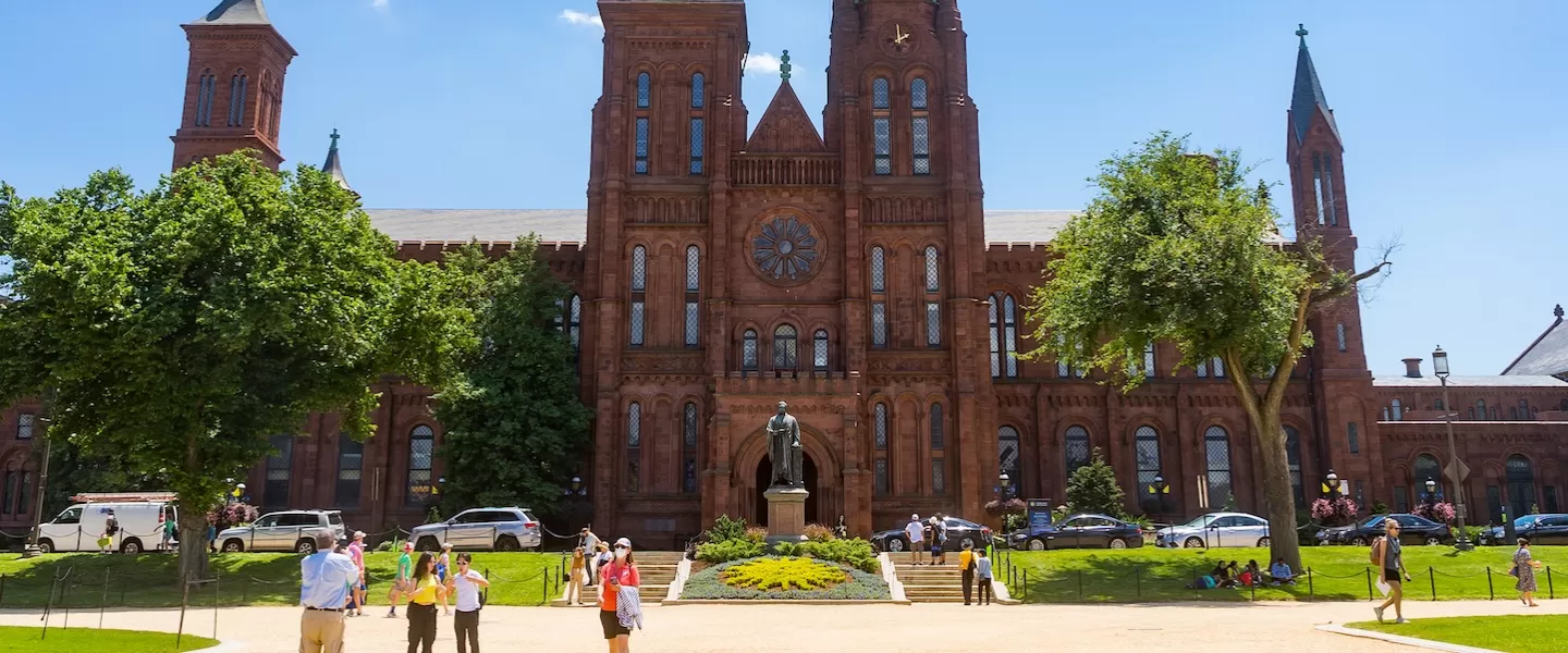 Visitors stroll across the sunny lawn in front of the iconic red sandstone Smithsonian Castle on the National Mall.