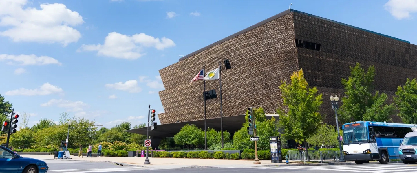 A view of the National Museum of African American History and Culture on a sunny day as cars pass by. . 