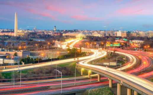  A vibrant view of Washington, DC, at twilight with light trails from vehicles on a highway interchange in the foreground and the Washington Monument standing tall in the cityscape.