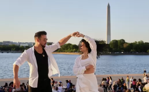 Two people dance with the Washington Monument in the background. 
