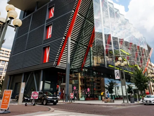 The modern glass and steel exterior of the International Spy Museum in Washington, DC, featuring red architectural accents and pedestrians along the street.