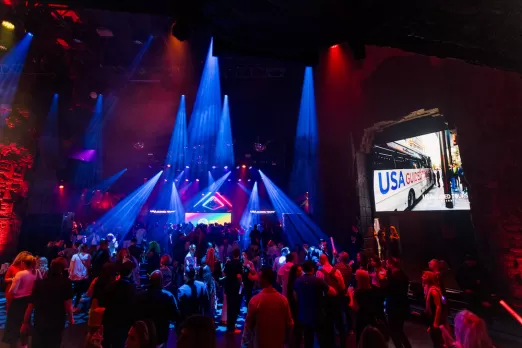 A lively crowd enjoys a night of music and dancing under dynamic lighting at a vibrant event, with a large screen displaying "USA Guided Tours" in the background.