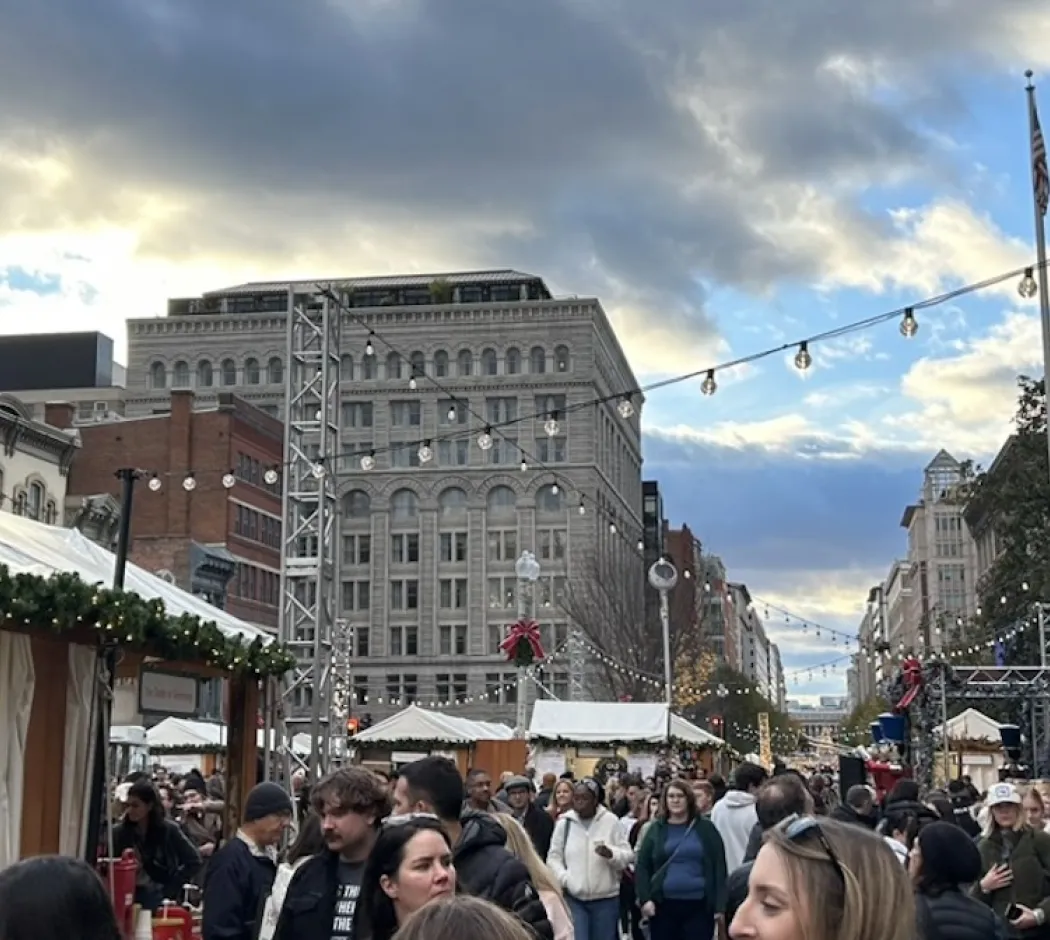 Holiday market scene in Downtown DC with crowds, festive decorations, and string lights.